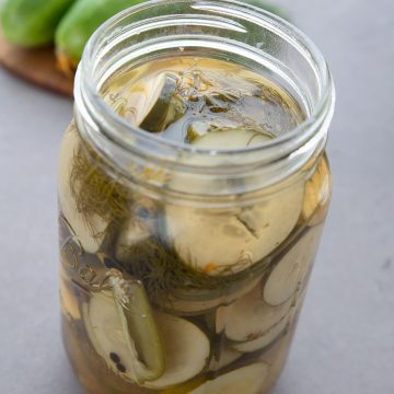 En krukke med keto kjøleskap pickles foran et skjærebrett med agurker.