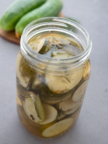 A jar of keto refrigerator pickles in front of a cutting board with cucumbers on it.