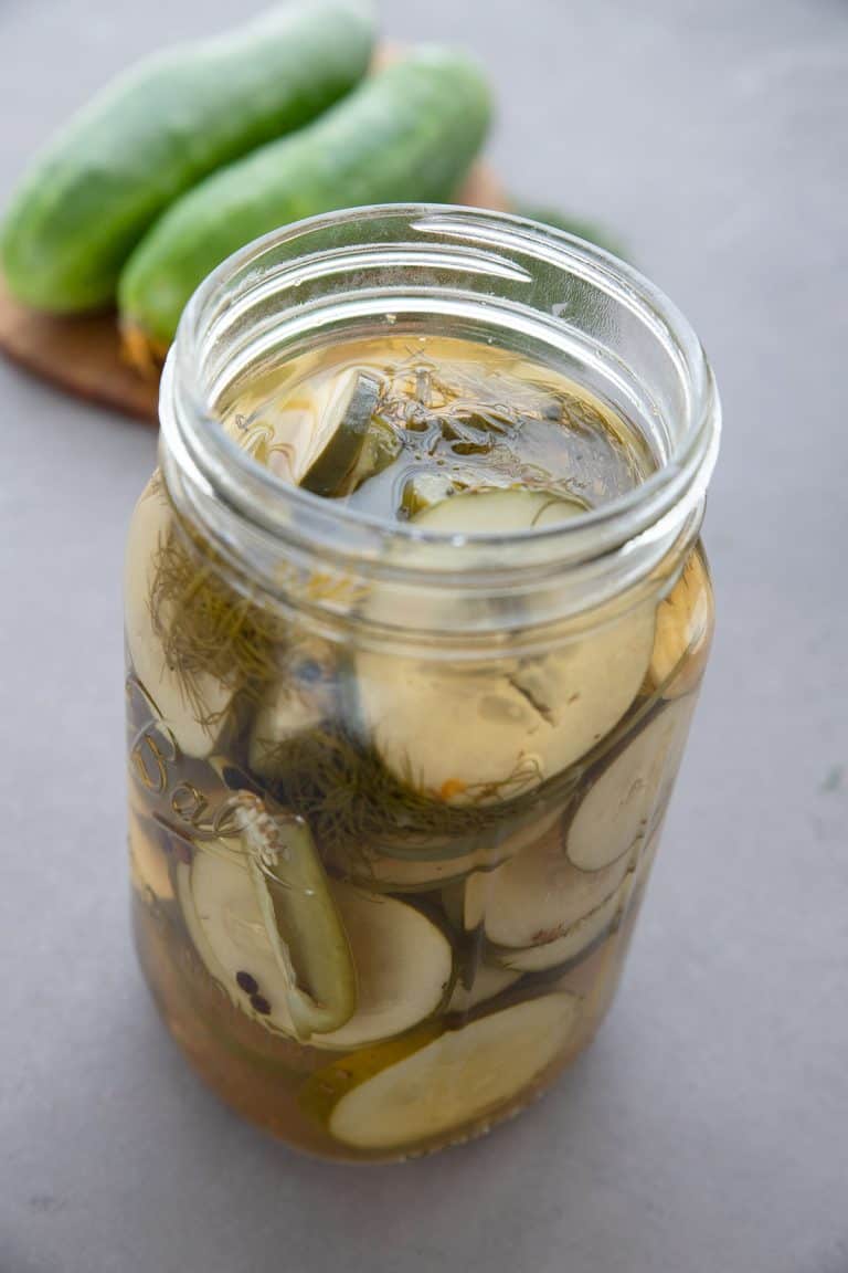 A jar of keto refrigerator pickles in front of a cutting board with cucumbers on it.