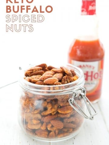 Titled Image of a jar of Keto Buffalo Roasted Nuts with a bottle of hot sauce in behind
