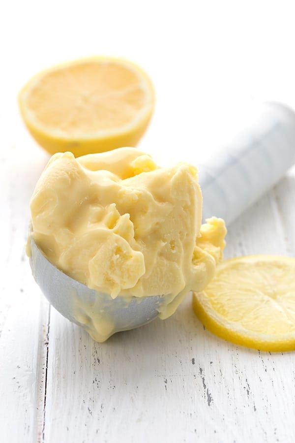 Lemon curd ice cream in an ice cream scoop with lemon halves and slices around it.
