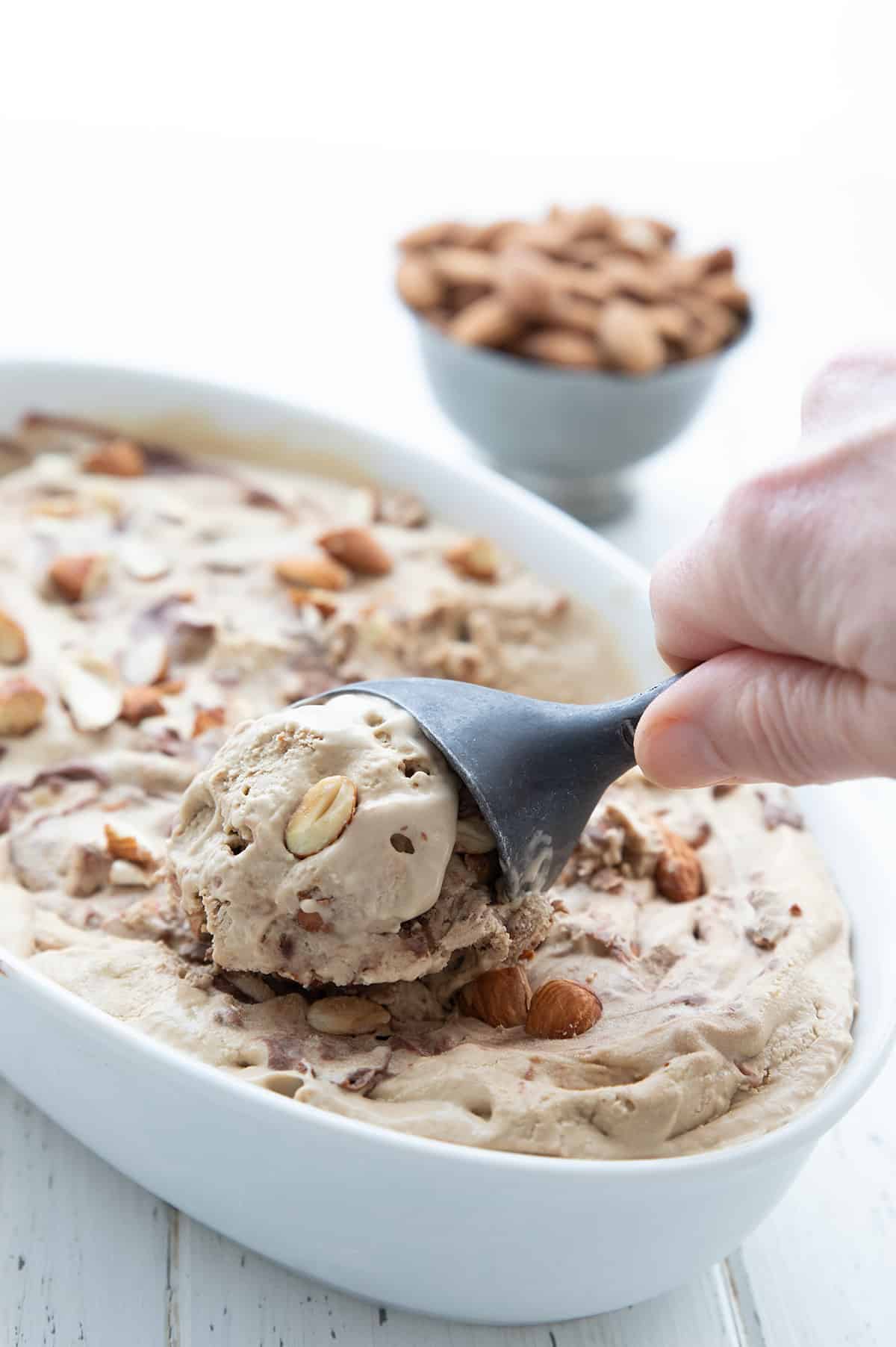 Keto Jamoca Almond Fudge Ice Cream being scooped out of a white oval dish with an ice cream scoop.