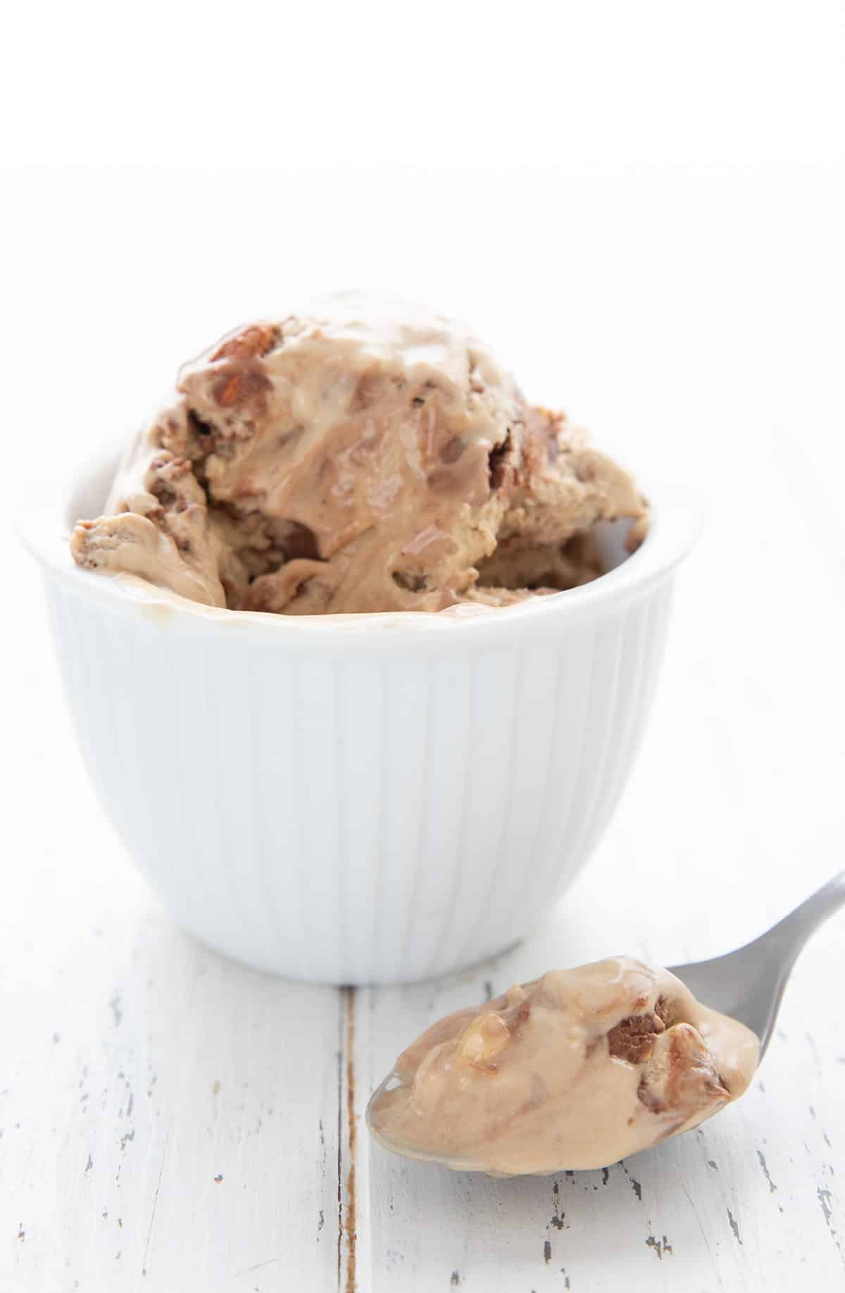 A bowl of keto mocha fudge ice cream on a white table, with a spoonful in the foreground. 