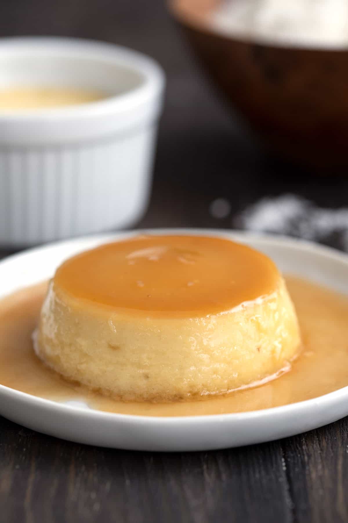 Keto flan with sugar-free caramel on a white plate on a dark brown wooden table. 