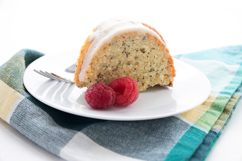 A slice of low carb lemon poppyseed cake on a white plate with a plaid napkin
