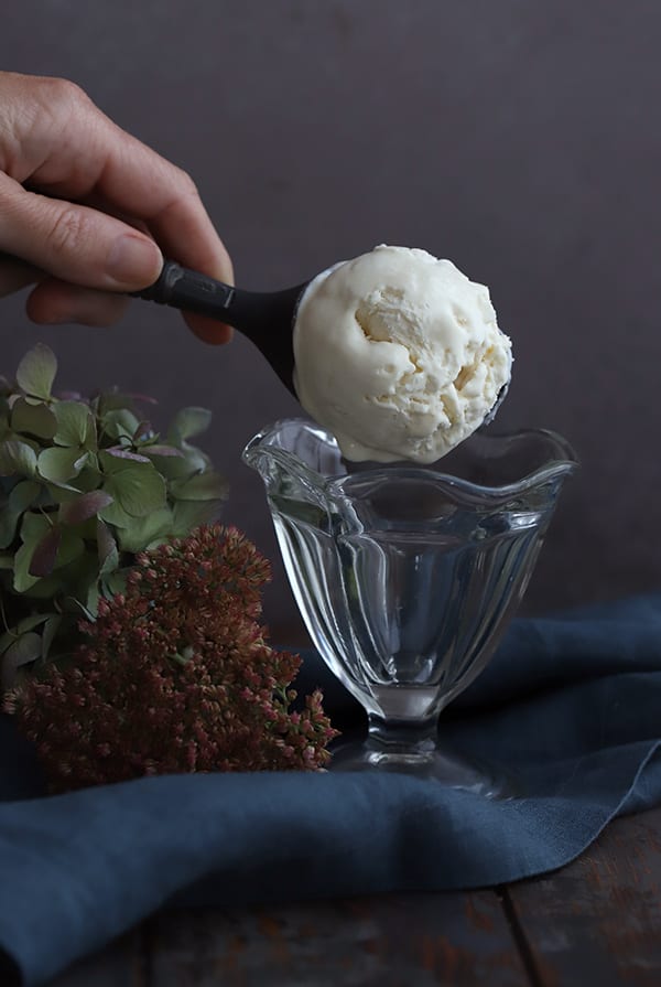 Scooping keto vanilla ice cream into a glass ice cream dish with flowers in the background