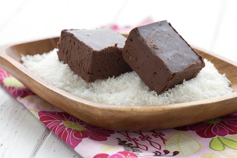 Two squares of dairy free chocolate in a wooden bowl filled with shredded coconut.