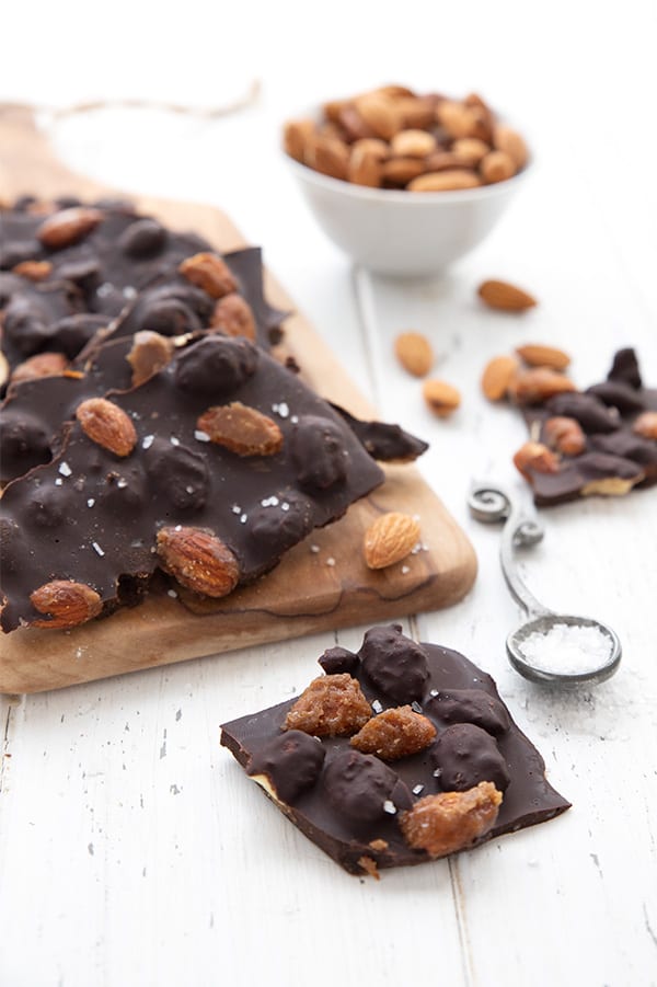 Keto chocolate bark with almonds and sea salt on a wooden cutting board with a bowl of almonds in the background.