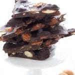 Titled image of keto almond bark on a white cake stand with almonds strewn around.
