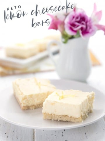 Keto lemon cheesecake bars on a white plate with a vase of flowers in the background.