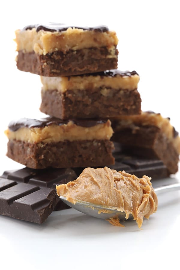 Low carb buckeye brownies in a stack behind some dark chocolate and a scoop of peanut butter
