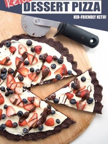 Top down image of keto cookie pizza on a pizza board with a slice cut out.