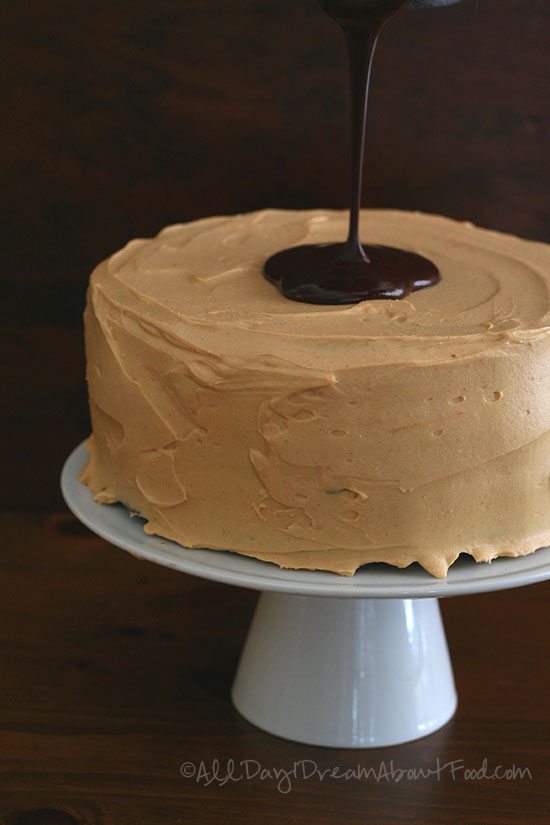 sugar free chocolate ganache being poured over the top of a low carb chocolate peanut butter layer cake