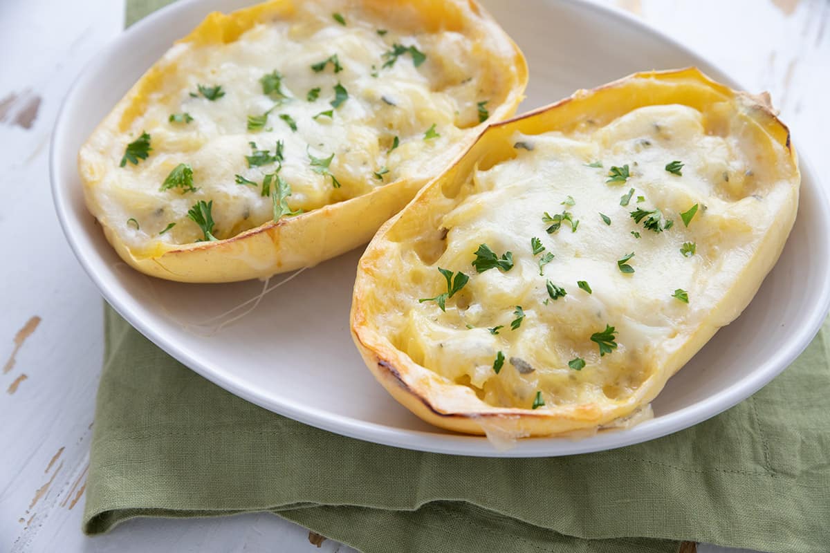 Two halves of a cooked spaghetti squash, filled with cheese, butter, and garlic, in an oval baking dish. 