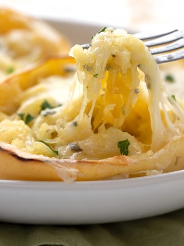 A close up shot of a fork lifting cheesy baked spaghetti squash out of the shell.