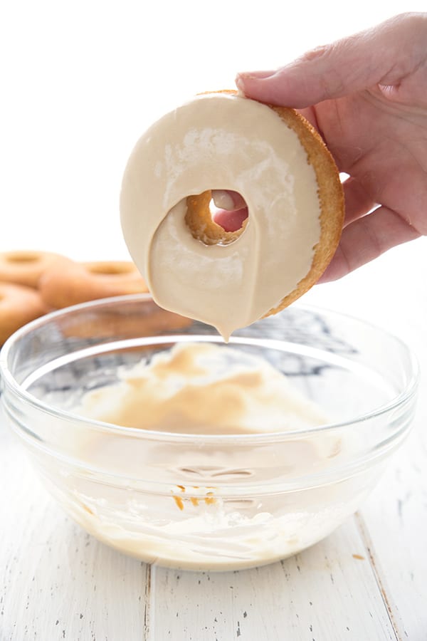 A hand dipping keto donuts into maple glaze