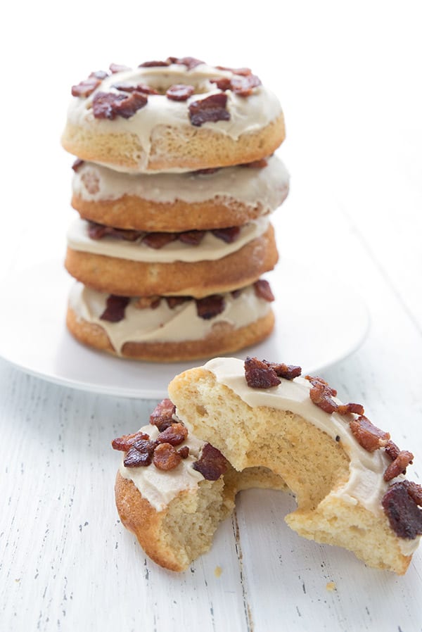A stack of maple bacon donuts on a white table, with one broken open in front. 