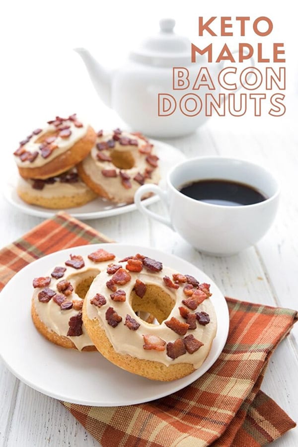Titled image of keto Maple Bacon Donuts on a white plate, over a brown plaid napkin on a white table. A coffee cup and pot are in the background, along with another plate full of donuts