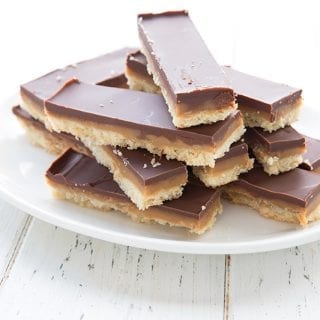 A white plate full of cut up homemade Twix bars on a white table.