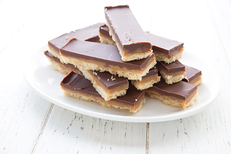 A white plate full of cut up homemade Twix bars on a white table.
