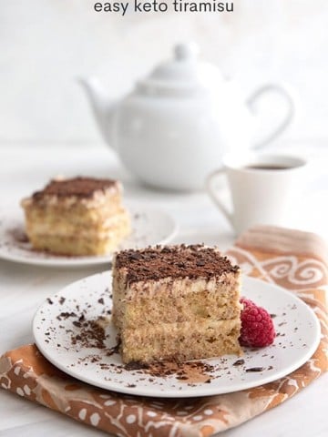 Titled image of keto tiramisu on white plates over a patterned napkin, with a white coffee cup and coffee pot in the background.