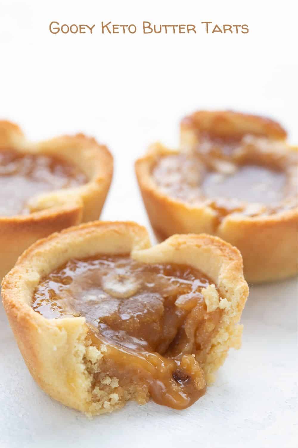 Titled image of a close up of keto butter tarts, with the front one broken open to show the gooey filling. 