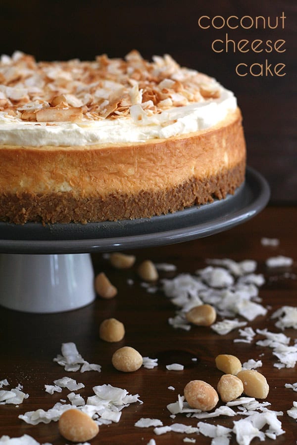 Keto Coconut Cheesecake on a cake stand with nuts and coconut around it.
