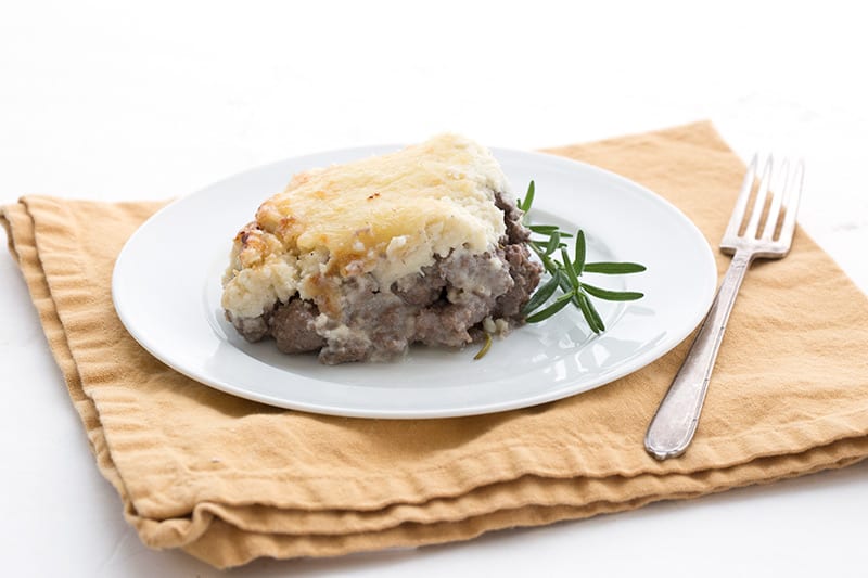 A piece of cauliflower shepherd's pie on a white plate with a sprig of rosemary
