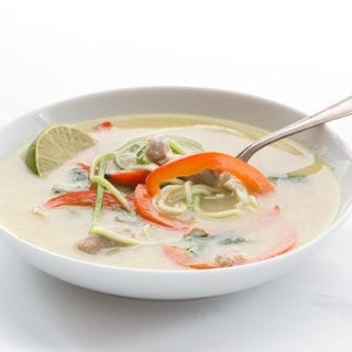 A white bowl filled with chicken zoodle soup on a white background