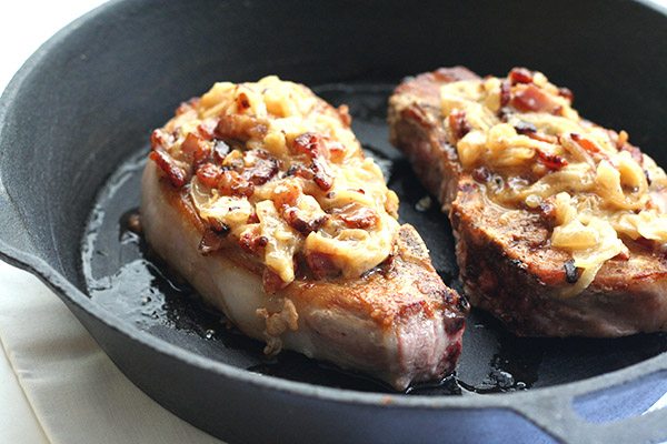 bacon and onion smothered pork chops in a cast iron skillet