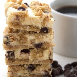 A stack of chocolate chip cheesecake bars with a cup of coffee in behind.