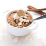 A single snickerdoodle mug cake with a spoon digging into it, with two cinnamon sticks in the background.