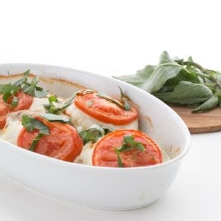 Easy Caprese Chicken in an oval white dish with basil in the background