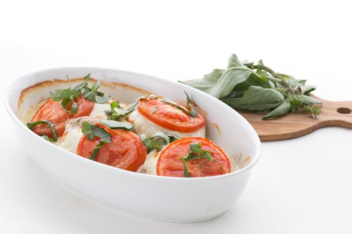Easy Caprese Chicken in an oval white dish with basil in the background
