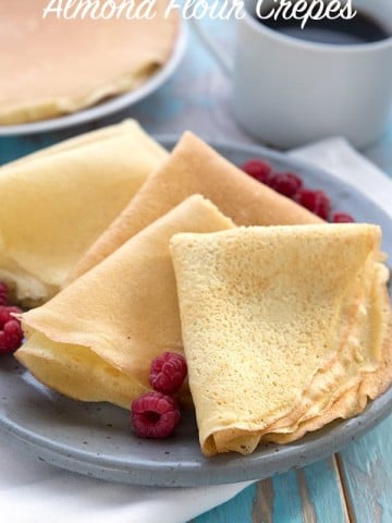 Keto almond flour crepes folded up on a grey plate, with a cup of coffee in behind.