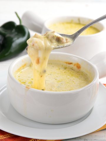 A spoon lifting gooey melted cheese out of a bowl of Chile Relleno Chicken Soup