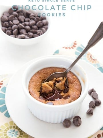 Titled image of a keto deep dish chocolate chip cookie in a white ramekin, with a spoon digging into it and a bowl of chocolate chips in the background.