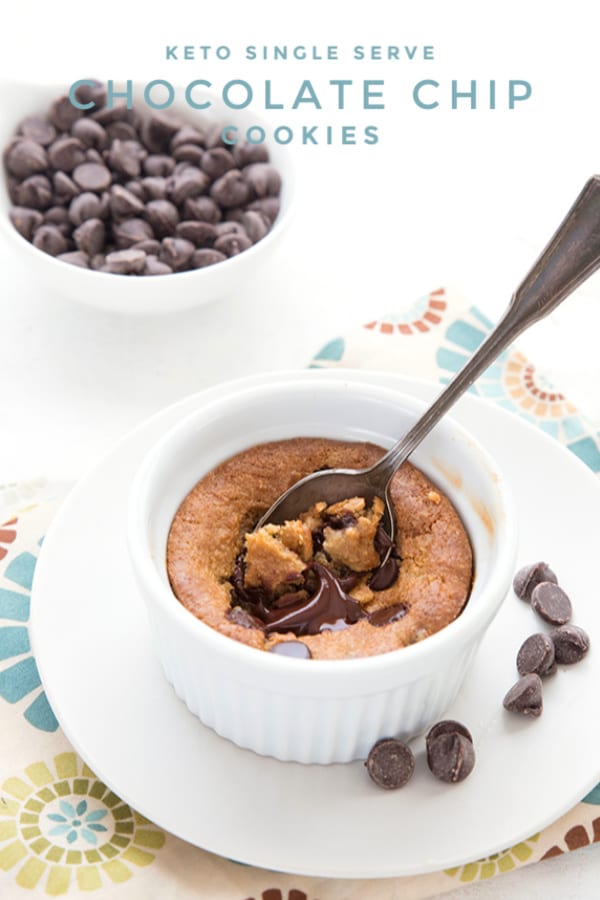 Titled image of a keto deep dish chocolate chip cookie in a white ramekin, with a spoon digging into it and a bowl of chocolate chips in the background. 