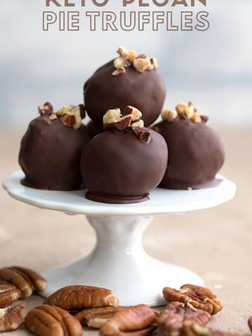 Titled image of keto pecan pie truffles on a small white cake stand with pecans strewn around.