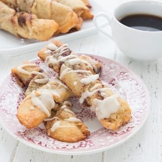 Keto cinnamon twists on a red patterned plate on a white wooden table. A cup of coffee and more cinnamon twists in the background.