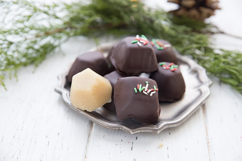 Chocolate dipped keto marzipan truffles on a pewter plate with cedar boughs around it. 