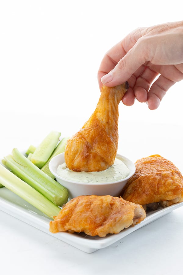 A Buffalo chicken drumstick being dipped into bleu cheese dressing. 