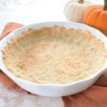 A baked low carb pie crust on an orange napkin with small pumpkins in the background.