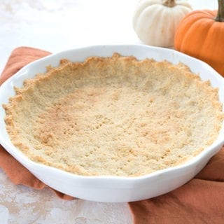 A baked low carb pie crust on an orange napkin with small pumpkins in the background.