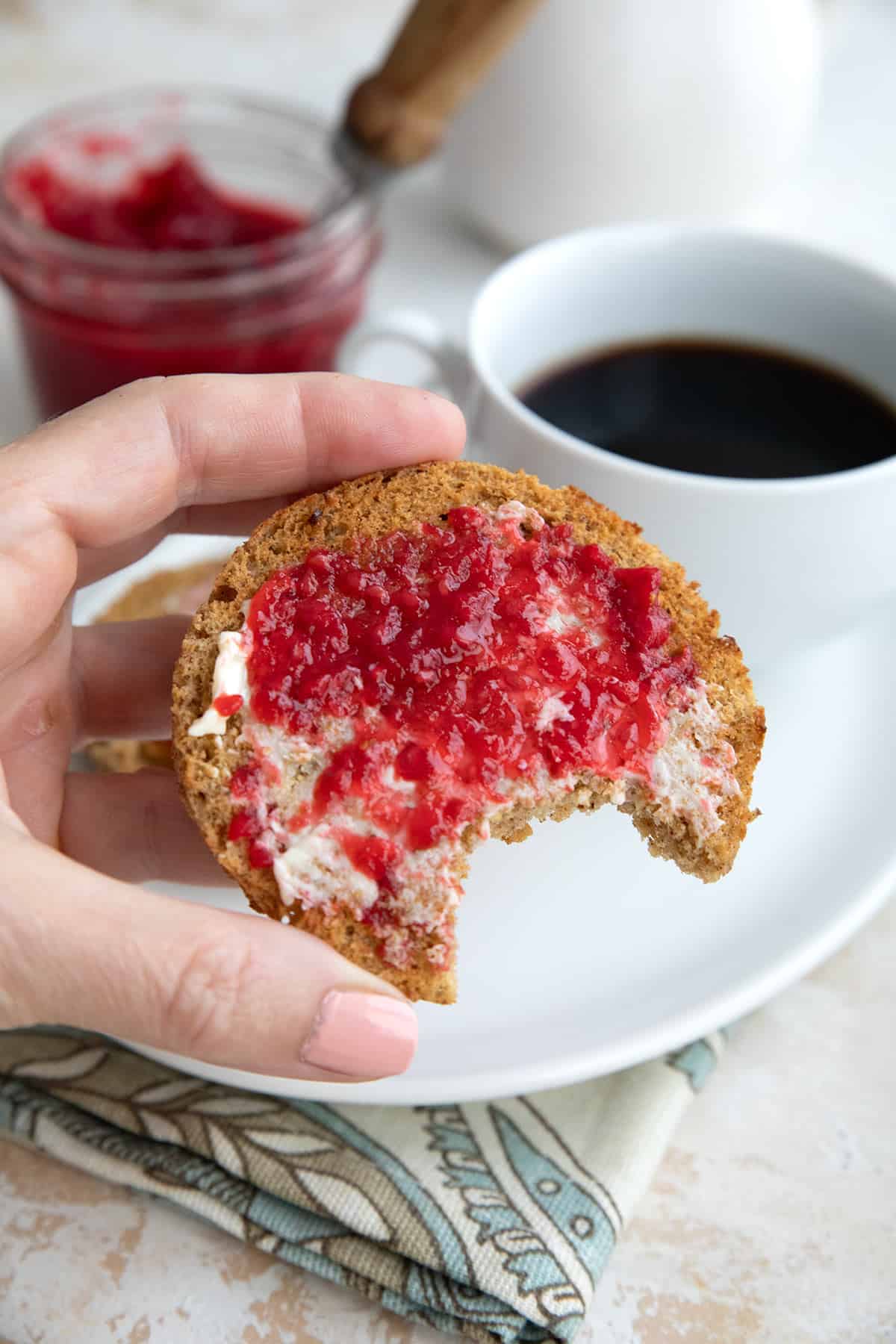 A hand holding up a Keto English Muffin with butter and jam on it.