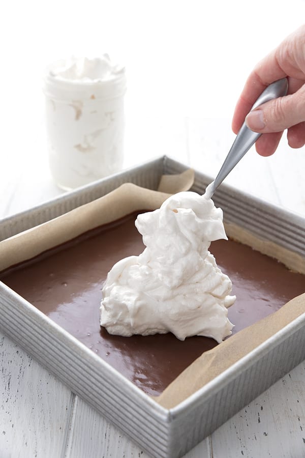 Spooning keto meringue onto sugar-free s'mores bars