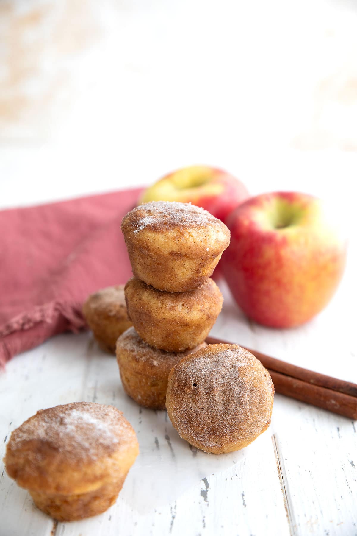 A stack of Keto Apple Cider Donut Bites with apples and cinnamon sticks in the background.