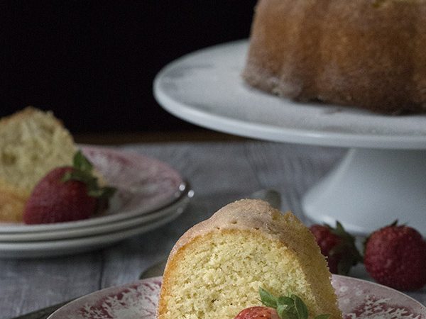 titled photo (and shown): Kentucky Butter Cake on a white cake stand with a slice of the low carb pound cake sitting on a dessert plate in front of it