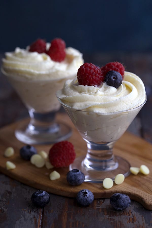 Two glass dessert cups filled with keto white chocolate mousse and fresh berries, sitting on a wooden cutting board.