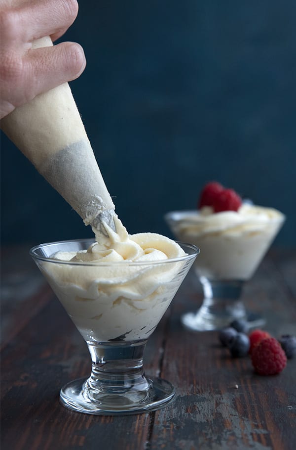 A piping bag piping keto cheesecake mousse into dessert cups